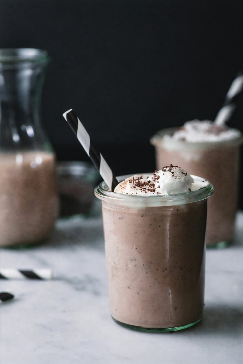 Gourmet chocolate milkshake with thick whipped cream and a black-and-white straw in a vertical jar composition.