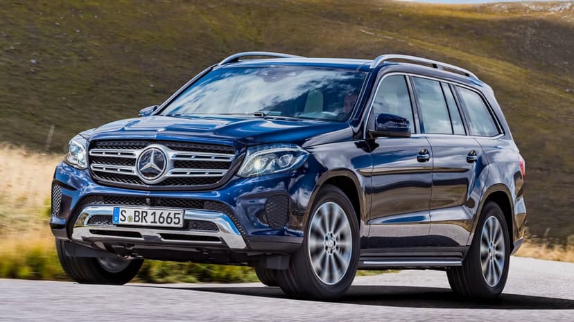 Blue Mercedes-Benz SUV driving on a mountain road with motion-blurred wheels and scenic hillside background.