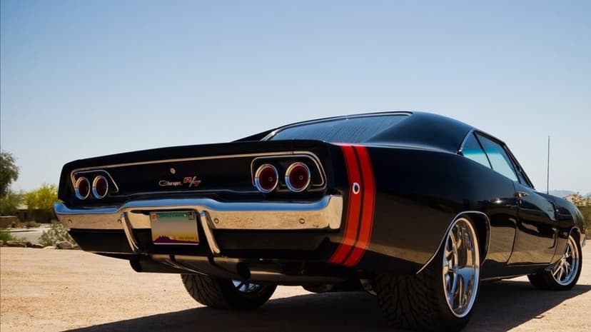 Black 1968 Dodge Charger R/T with red stripes on a desert path under a bright blue sky with chrome accents.
