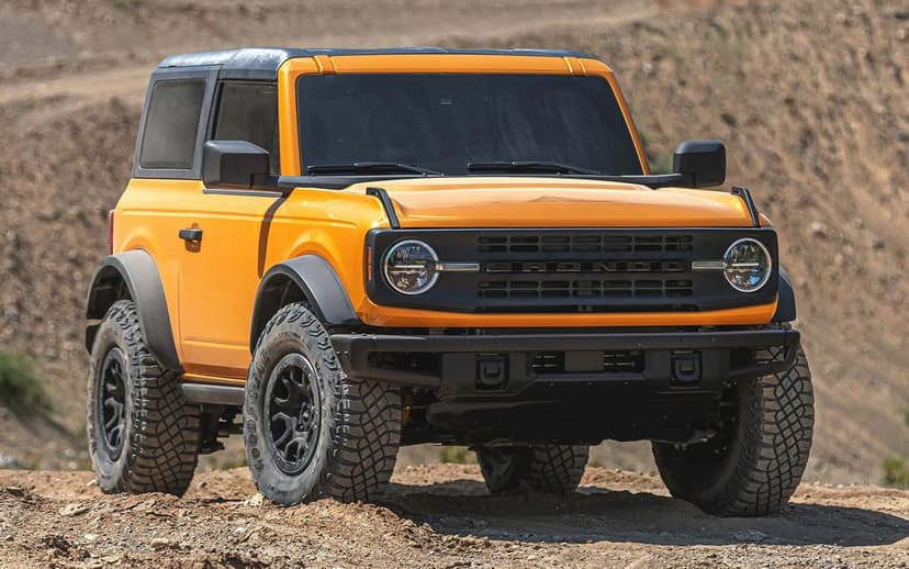 Orange two-door Ford Bronco with off-road tires parked on a dirt hill under bright daylight conditions.
