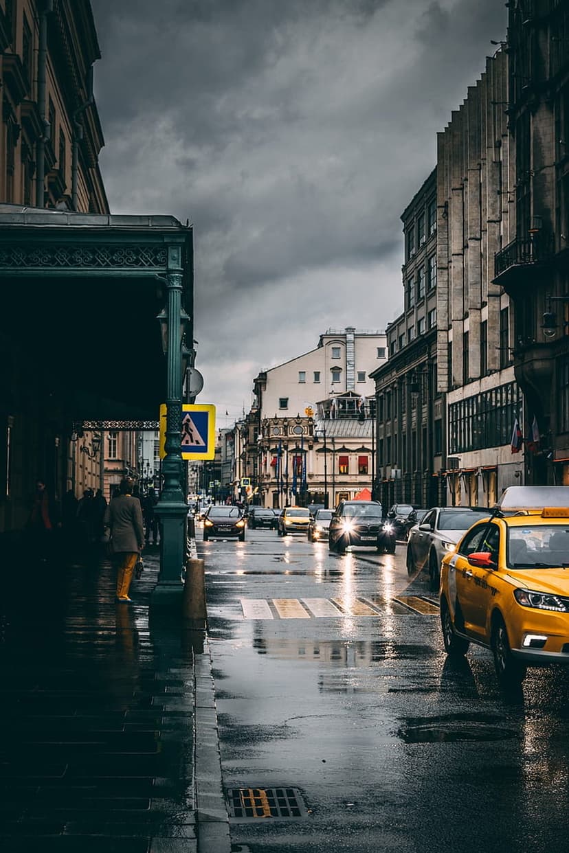 Yellow taxi driving on a wet city street with white pedestrian markings and headlights reflecting on damp asphalt.