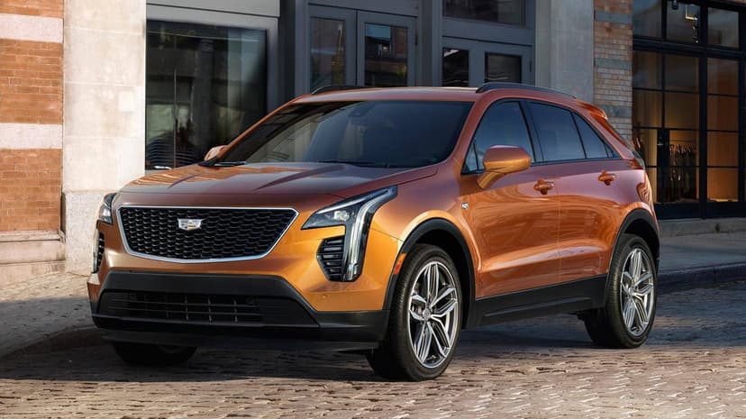Copper Cadillac XT4 SUV parked on a cobblestone street with brick buildings and glass storefronts behind it.