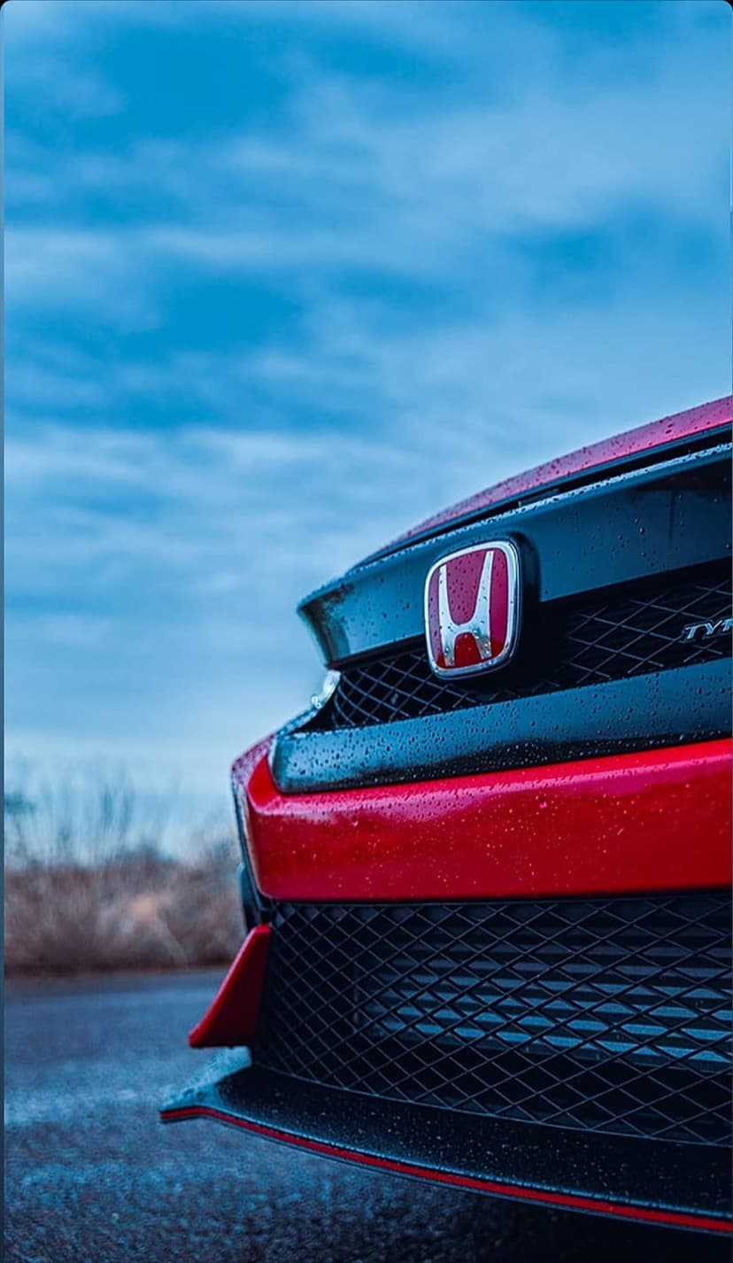 Red Honda emblem and honeycomb grille covered in tiny water droplets against a blurred street background.