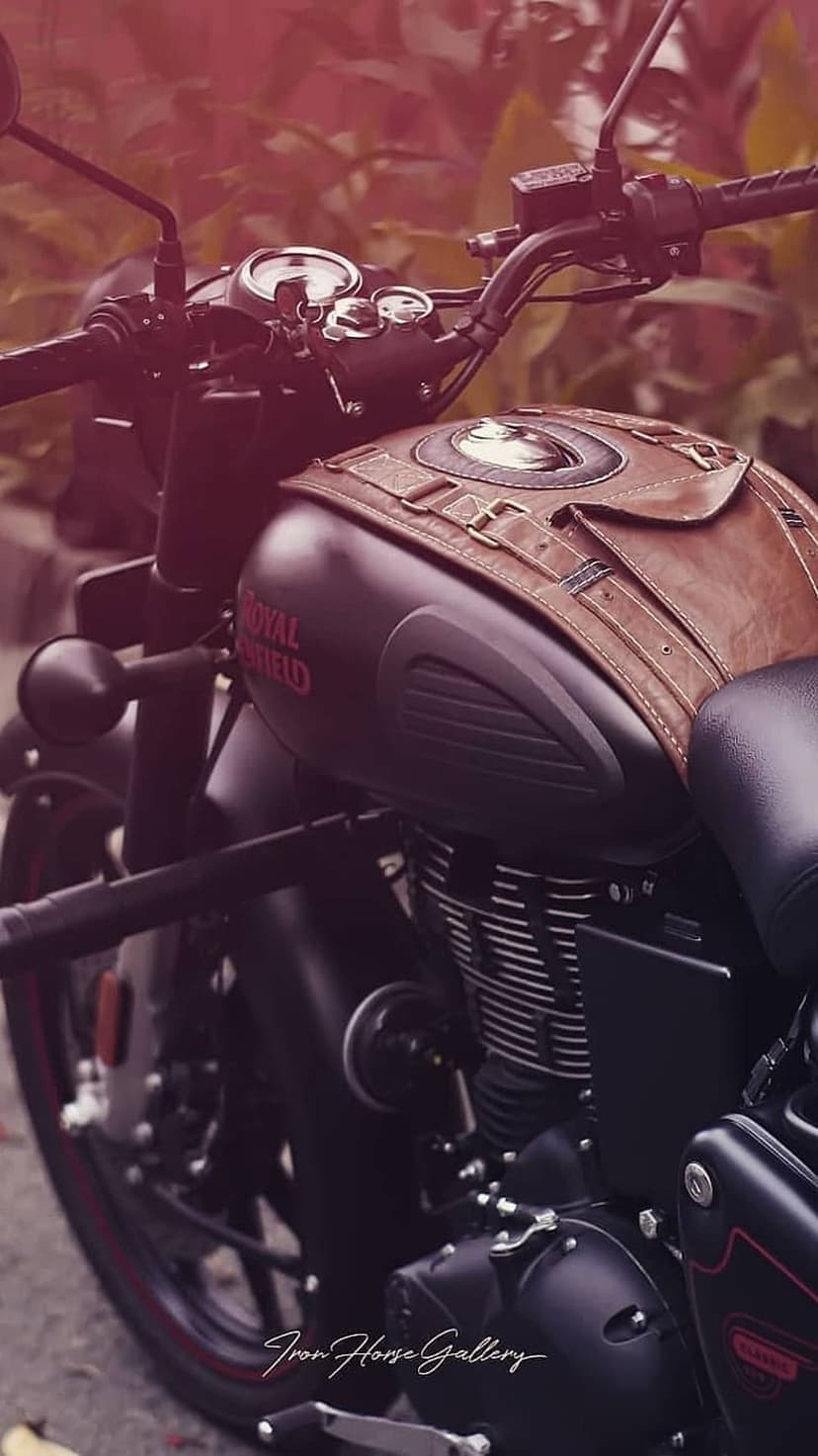 Royal Enfield motorcycle with a brown leather tank cover, matte black engine, and chrome handlebars in focus.