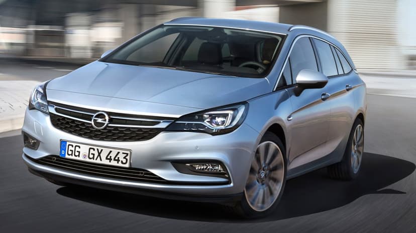 Silver Opel Astra Sports Tourer driving on a city road with motion blur on wheels and a blurred background.