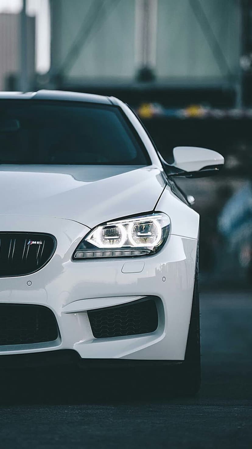 BMW M6 white luxury coupe front view featuring aggressive LED headlights and a black grille on an urban street.