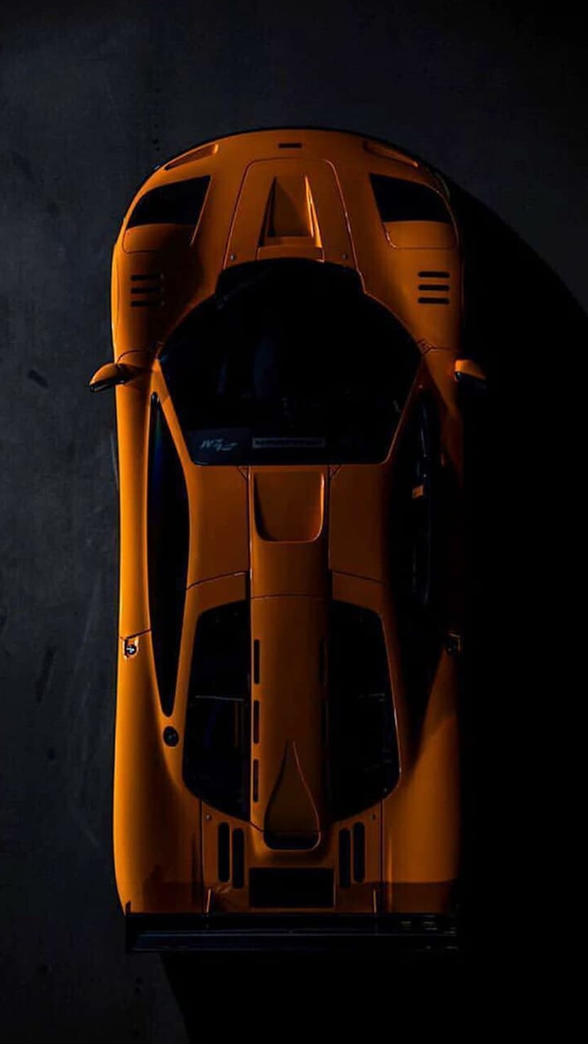 Orange McLaren F1 GTR race car seen from a top-down view with dramatic shadows on its aerodynamic body panels.