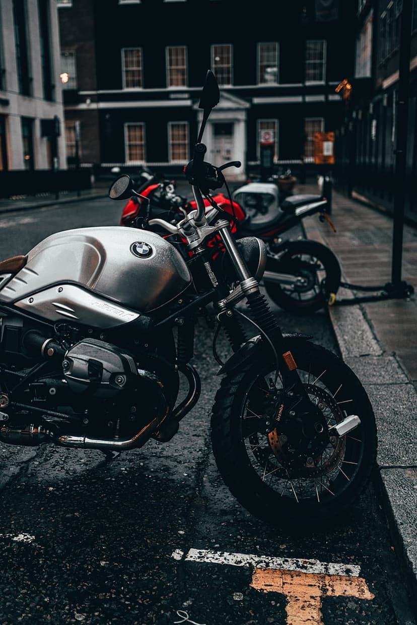 Silver BMW motorcycle with chrome engine parts stands on a wet street near blurred historic city architecture.