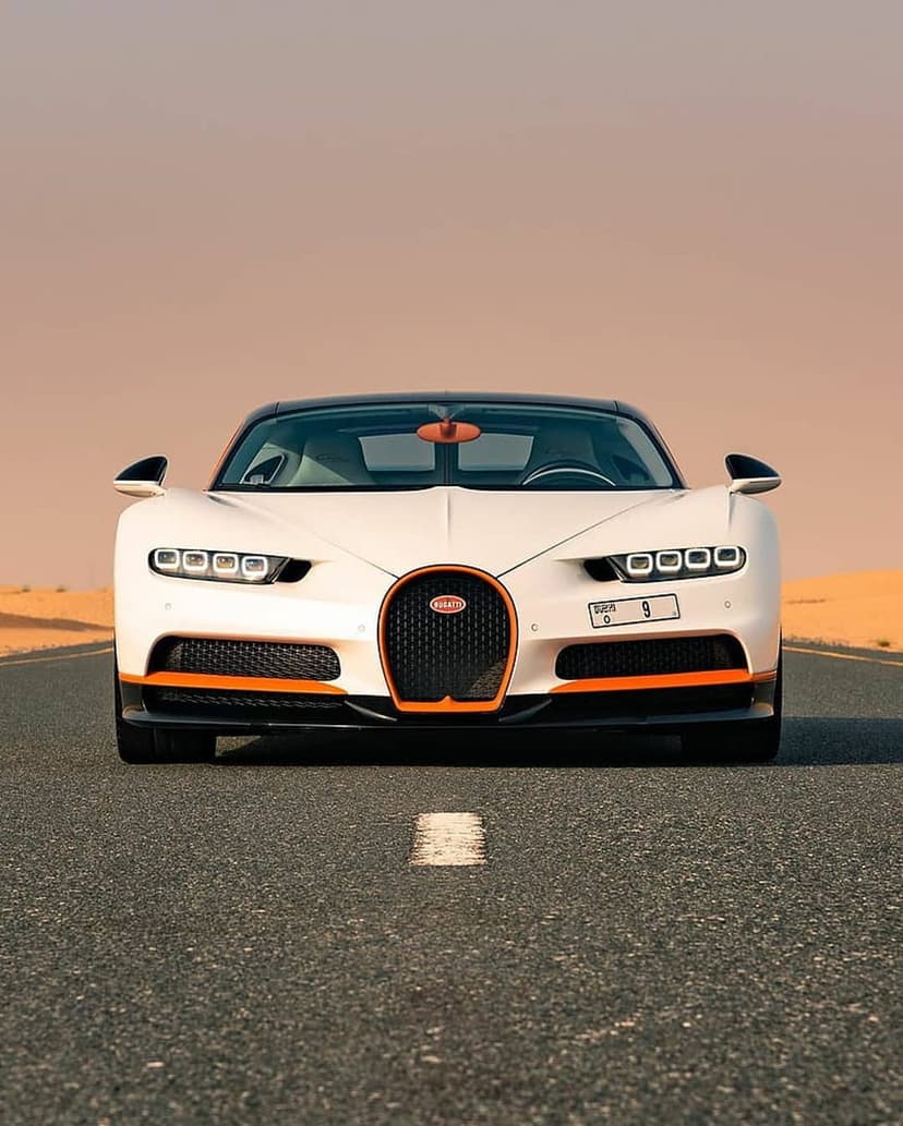 White Bugatti Chiron hypercar with orange accents on an asphalt desert road during golden hour sunset.