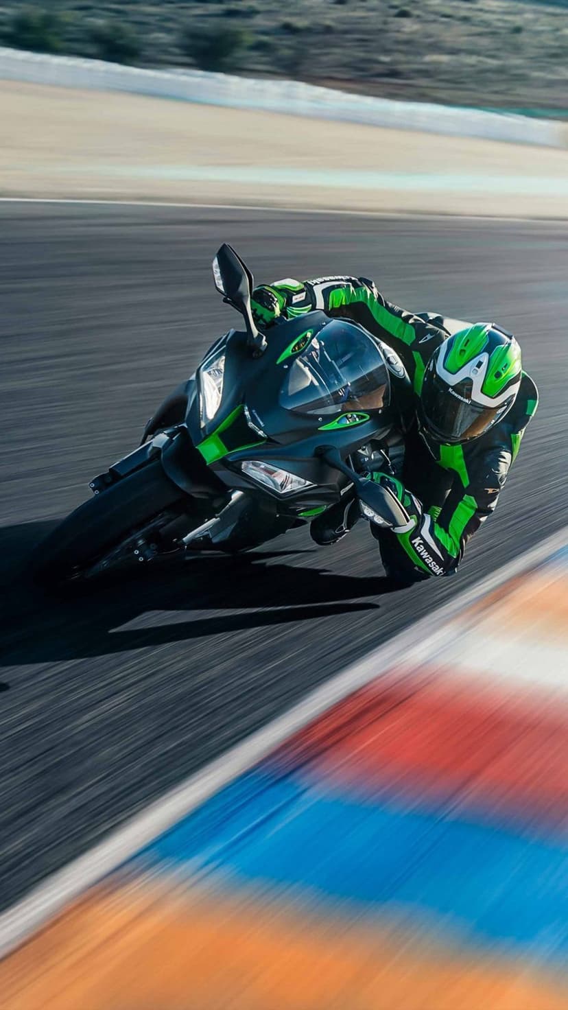 Kawasaki motorcycle rider in a green racing suit leans into a track corner with intense motion blur background.