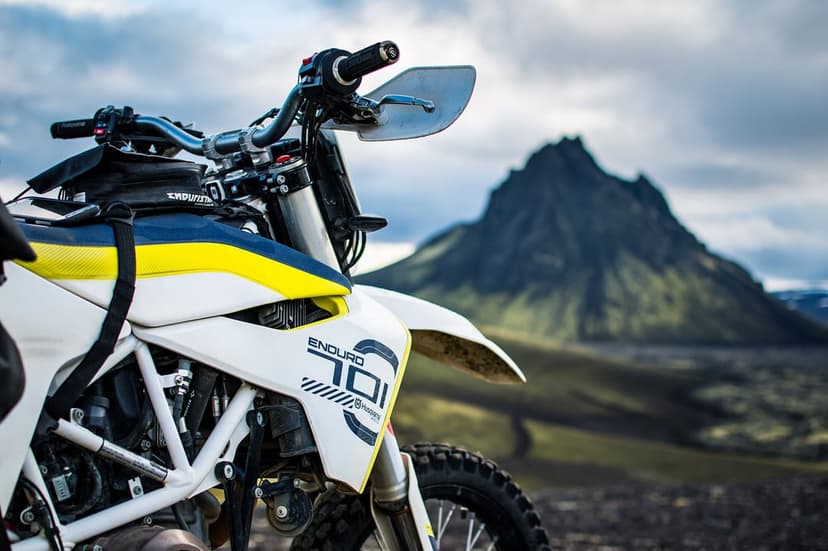 Husqvarna Enduro 701 motorcycle with a mossy volcanic mountain and cloudy sky in the background.