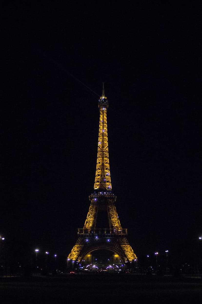 Eiffel Tower illuminated with golden lights against a dark night sky with soft blue sparkles and city glow.