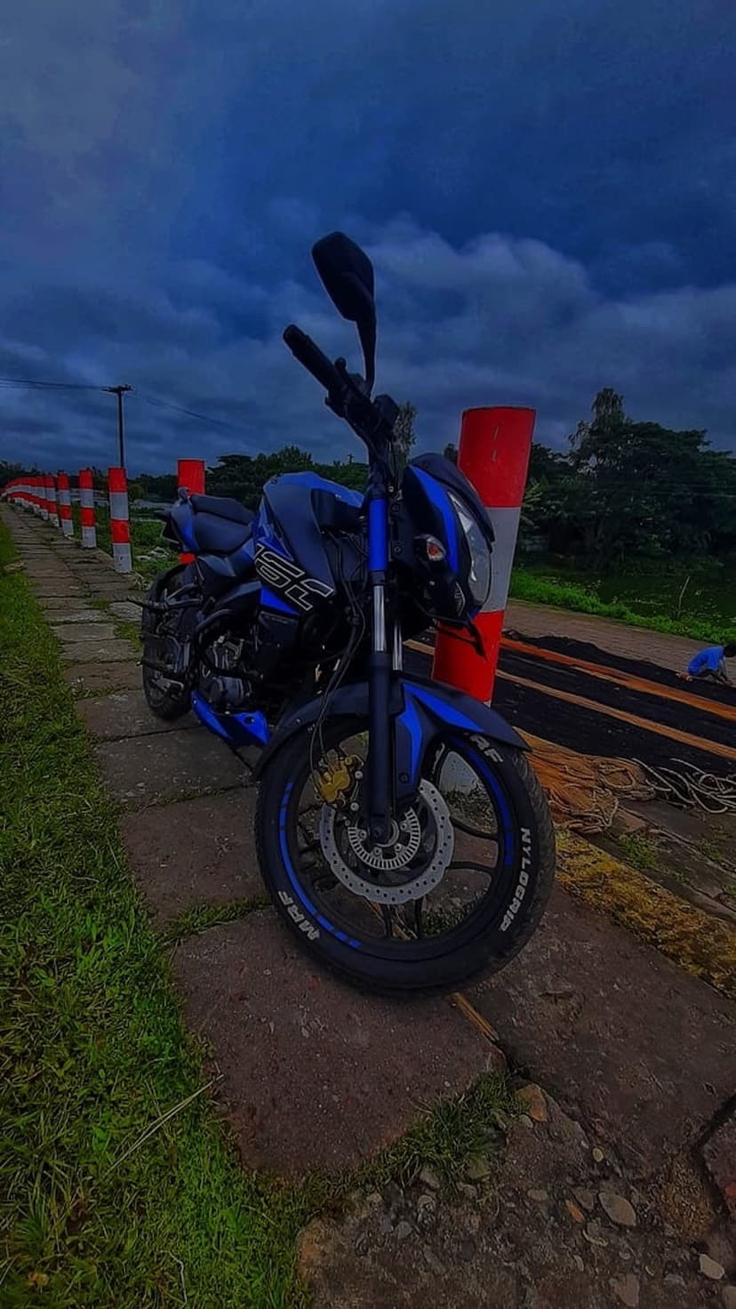 Blue and black sports bike parked on a paved path by a lake under a cloudy sky with red and white bollards.