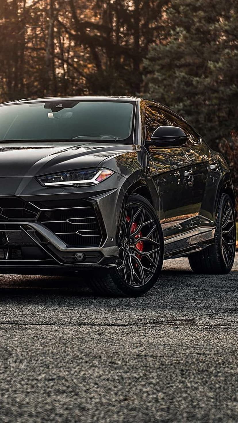 Black Lamborghini Urus SUV with sharp headlights and red brake calipers parked on a textured asphalt surface.