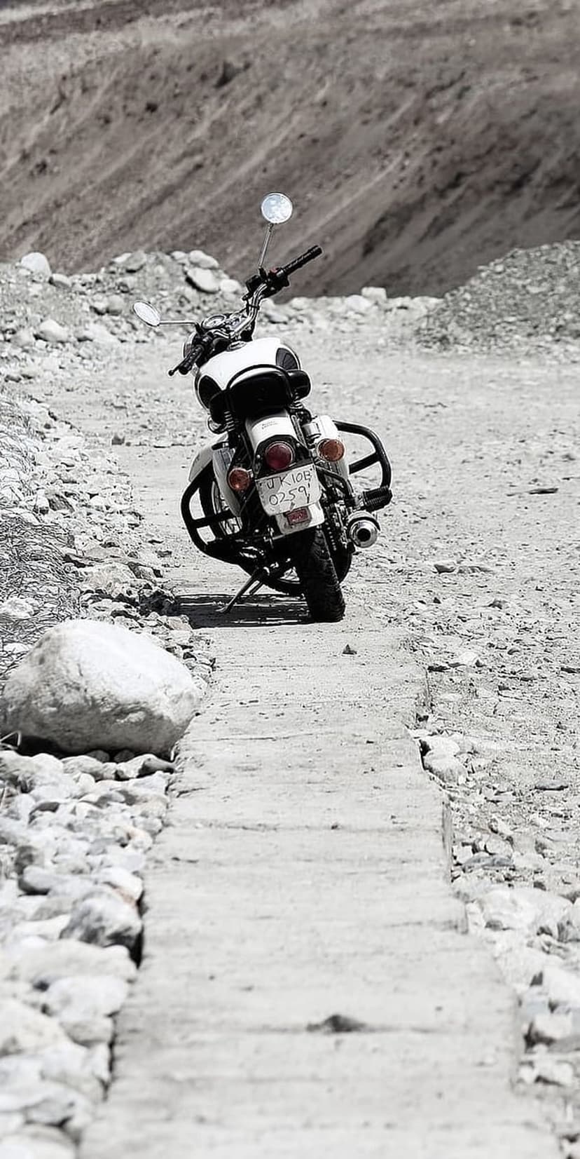 White motorcycle parked on a steep rocky mountain trail with grey scree slopes in the arid background.