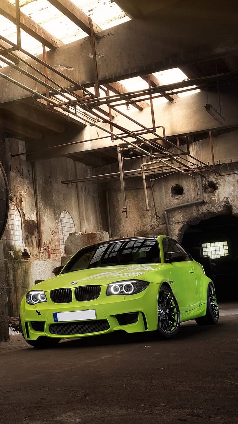 Lime green BMW coupe parked in a derelict industrial warehouse with concrete walls and overhead piping.