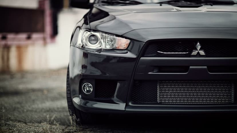 Front view of a dark grey Mitsubishi Lancer Evolution with projector headlights and a mesh grille.