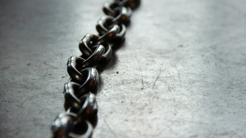 Interlocking polished steel chain links resting on a brushed gray metallic surface with soft background blur.