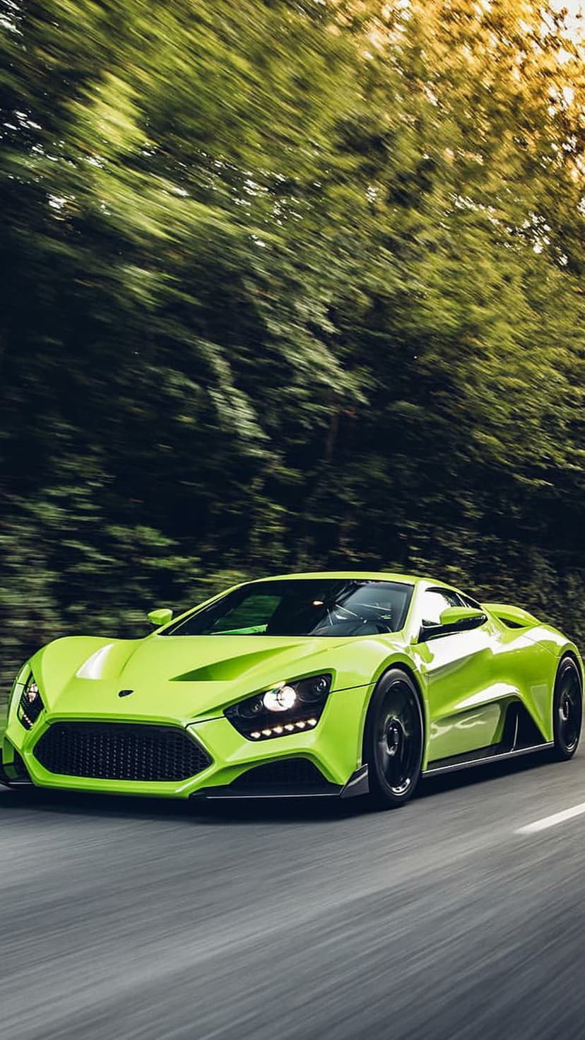 Zenvo TSR-S supercar in vibrant green speeds past a blurred forest backdrop on a paved mountain road.