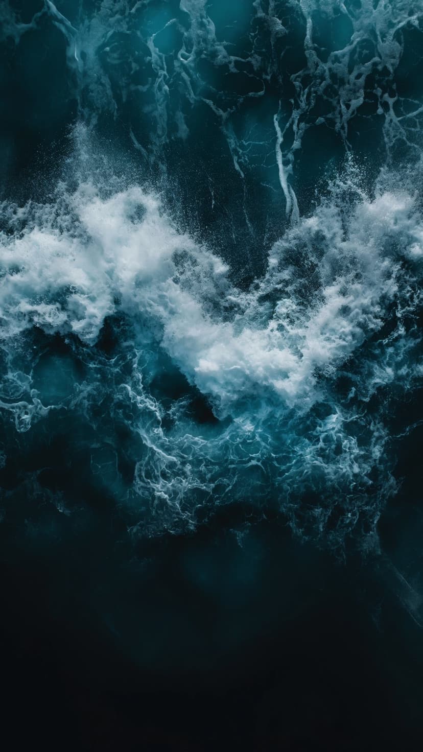 Deep blue ocean waves crash into white foam and swirling surf in a vertical top-down aerial perspective.