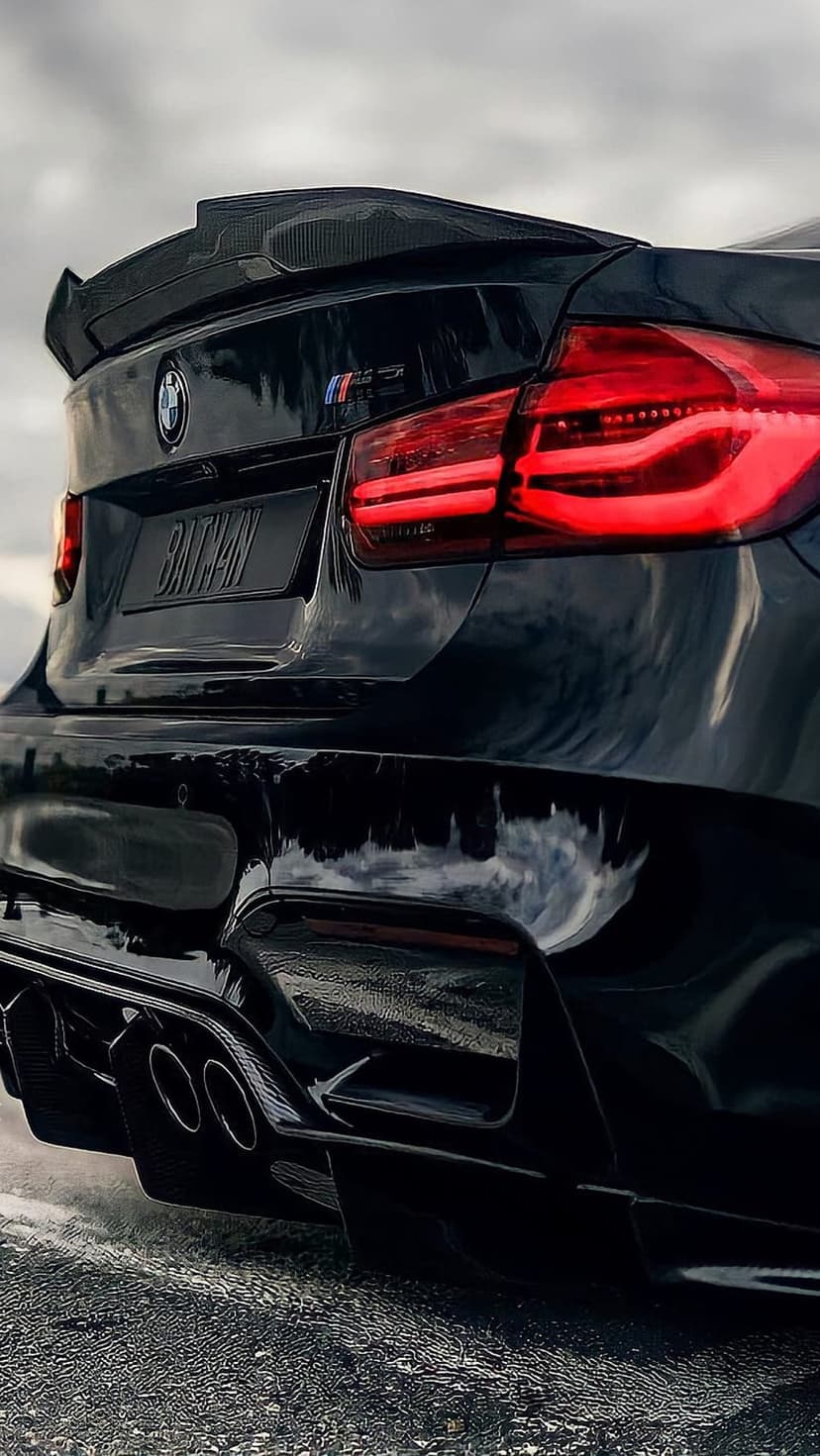 Black BMW M3 rear view featuring a carbon fiber spoiler, Batman license plate, and glowing red taillights.