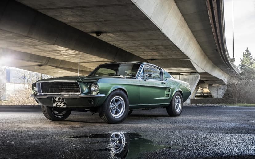 Dark green classic muscle car parked on wet asphalt under a concrete overpass with a reflective puddle.