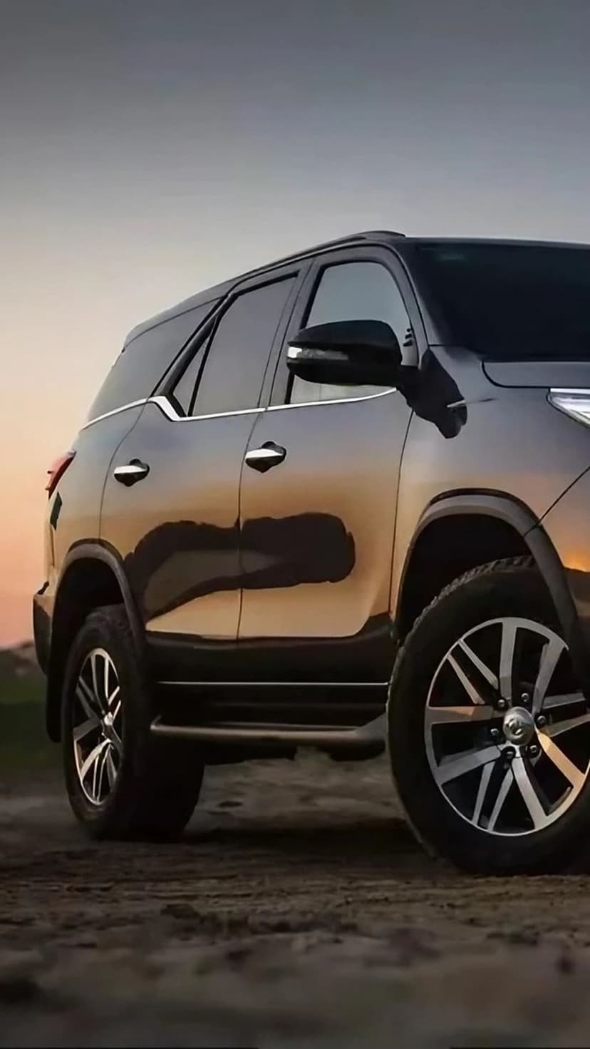 Black SUV parked on a dusty rural road at sunset with golden light reflecting off the metallic vehicle body.