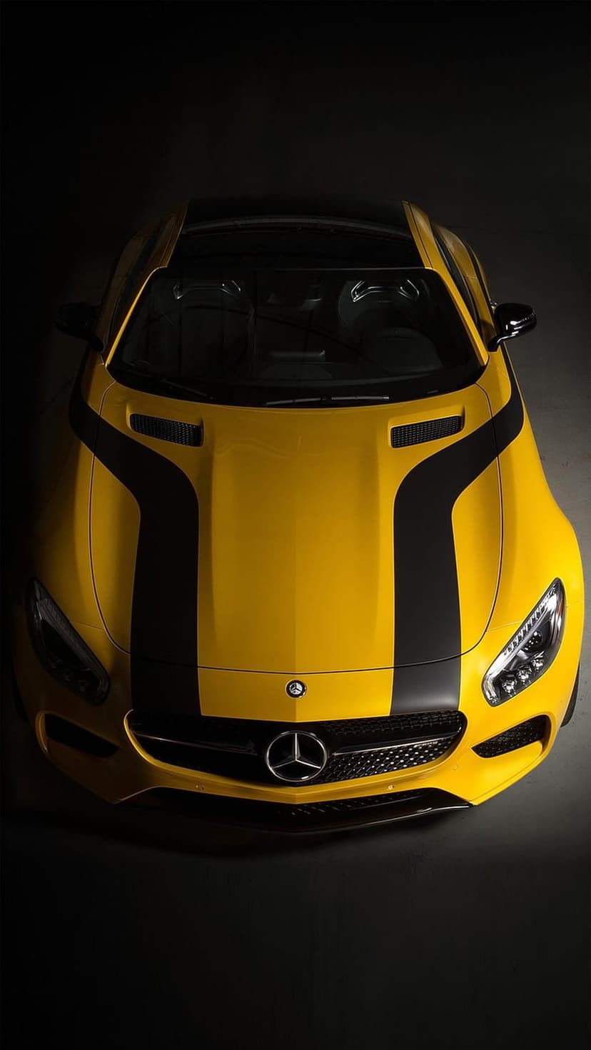 Yellow Mercedes-AMG GT S with black racing stripes captured from a top-down perspective against a dark background.