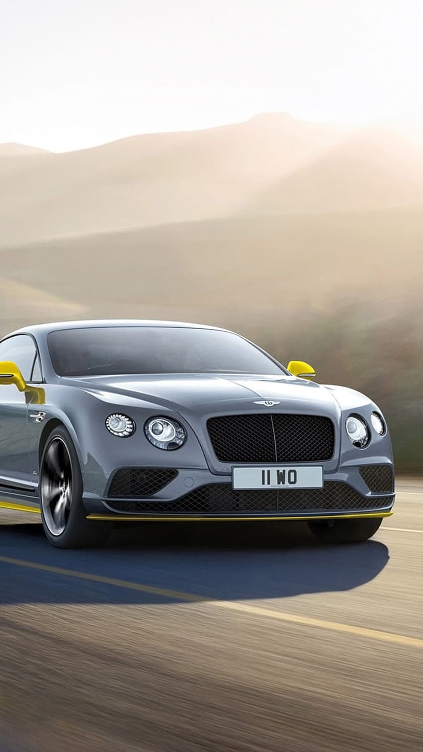 Bentley Continental GT in grey with yellow trim driving on a desert highway during a warm golden hour sunset.