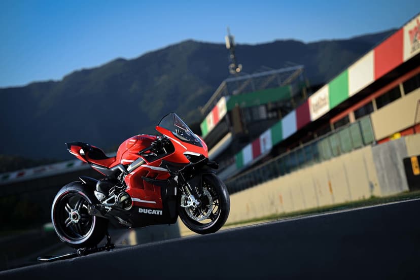 Red Ducati Superleggera V4 sportbike parked on a racetrack with Italian flag buildings and hills behind.