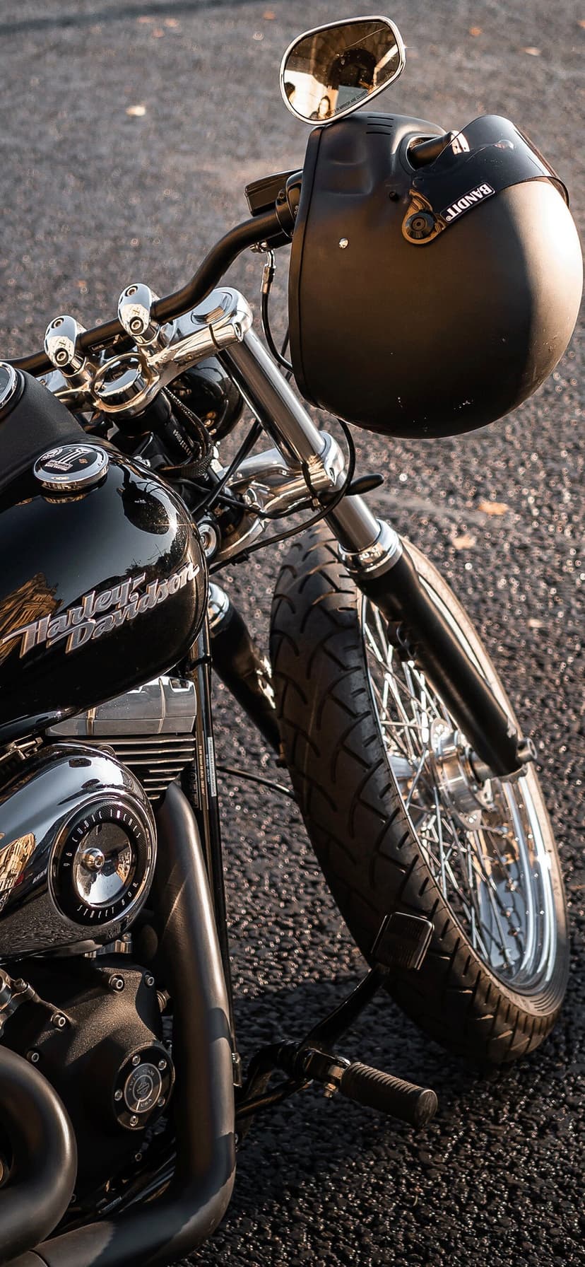 Black Harley-Davidson cruiser fuel tank and engine with a matte helmet hanging on handlebars over asphalt.