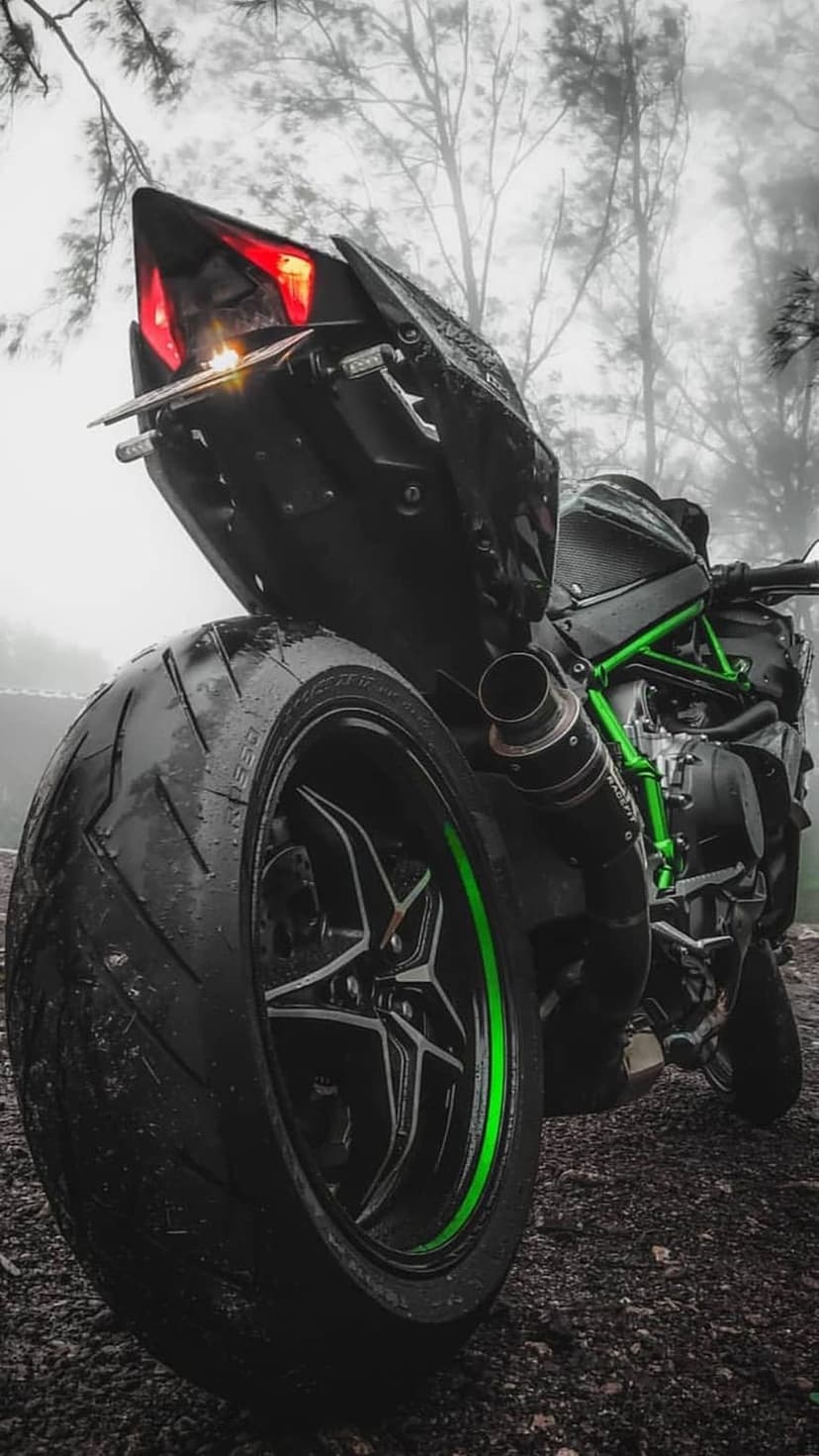 Kawasaki Ninja H2R motorcycle with its green frame parked on a wet gravel path in a dense, misty forest.