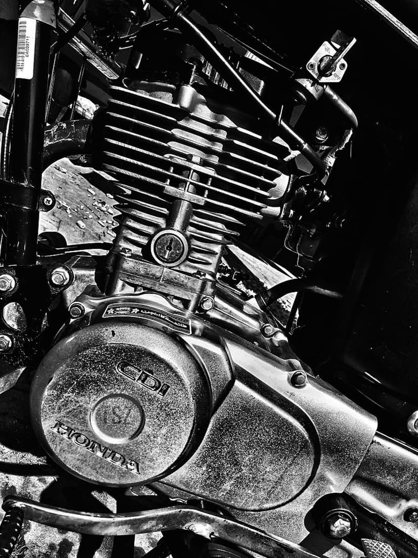 Honda motorcycle engine close-up showing ribbed cooling fins and chrome casing in high-contrast monochrome tones.