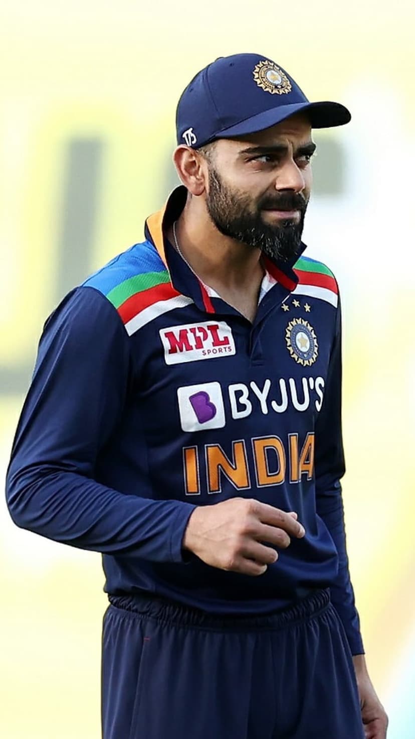 Virat Kohli wearing a blue Indian cricket cap and national team jersey with an intense facial expression.