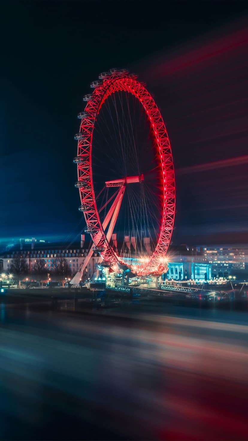London Eye ferris wheel illuminated in red at night over the River Thames with long exposure light trails.
