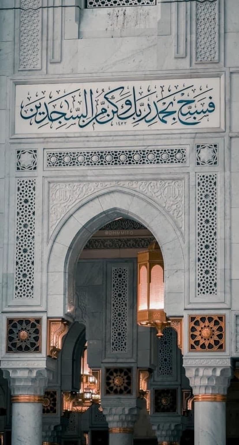 Ornate white marble archway featuring blue Arabic calligraphy and geometric carvings with warm interior lighting.