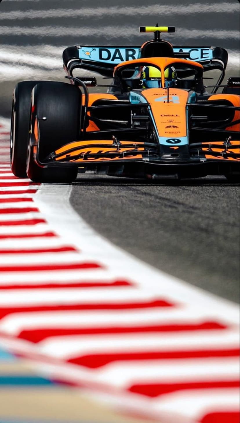 McLaren Formula 1 car in orange and blue livery speeds past red and white striped kerbing on a race circuit.