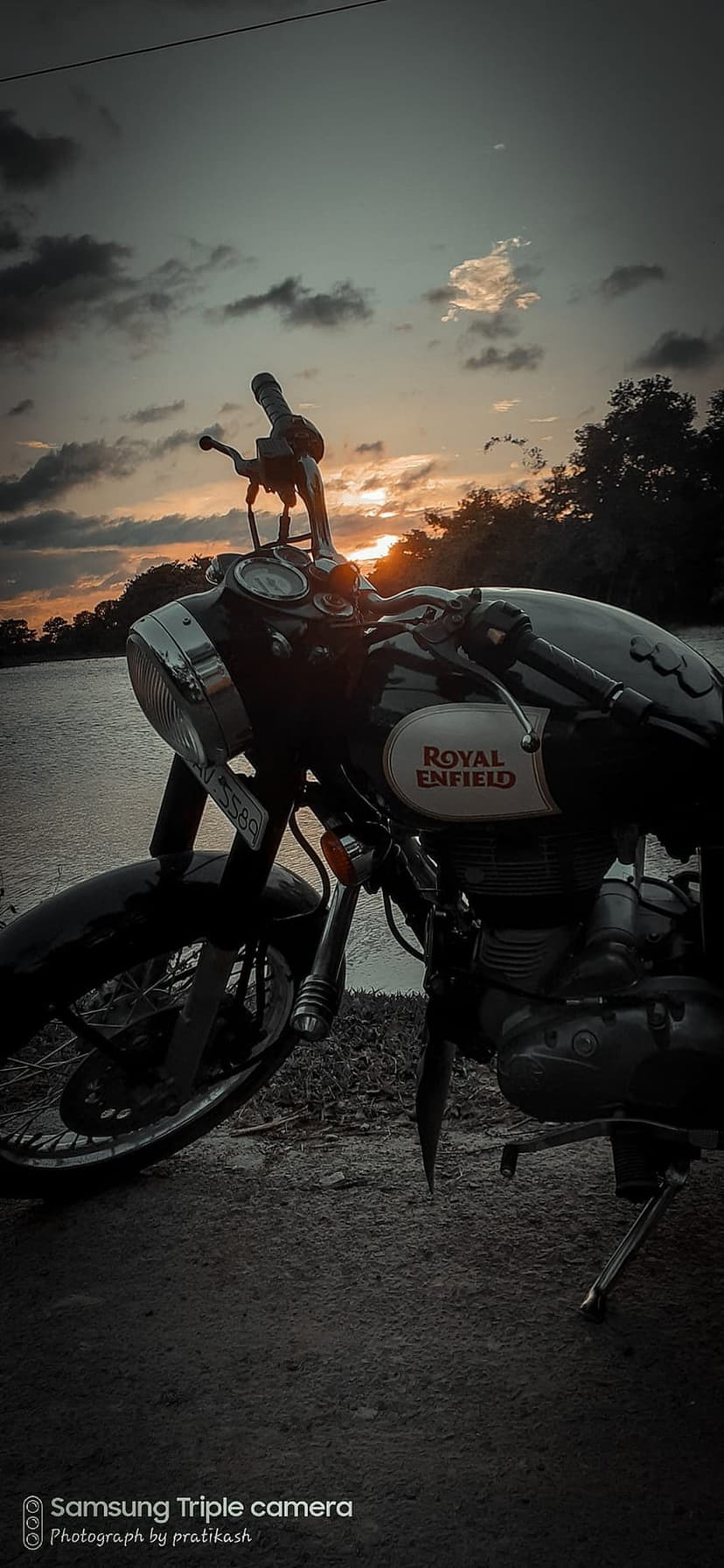 Royal Enfield motorcycle parked on a sandy beach under a vibrant orange sunset with reflections on the water.