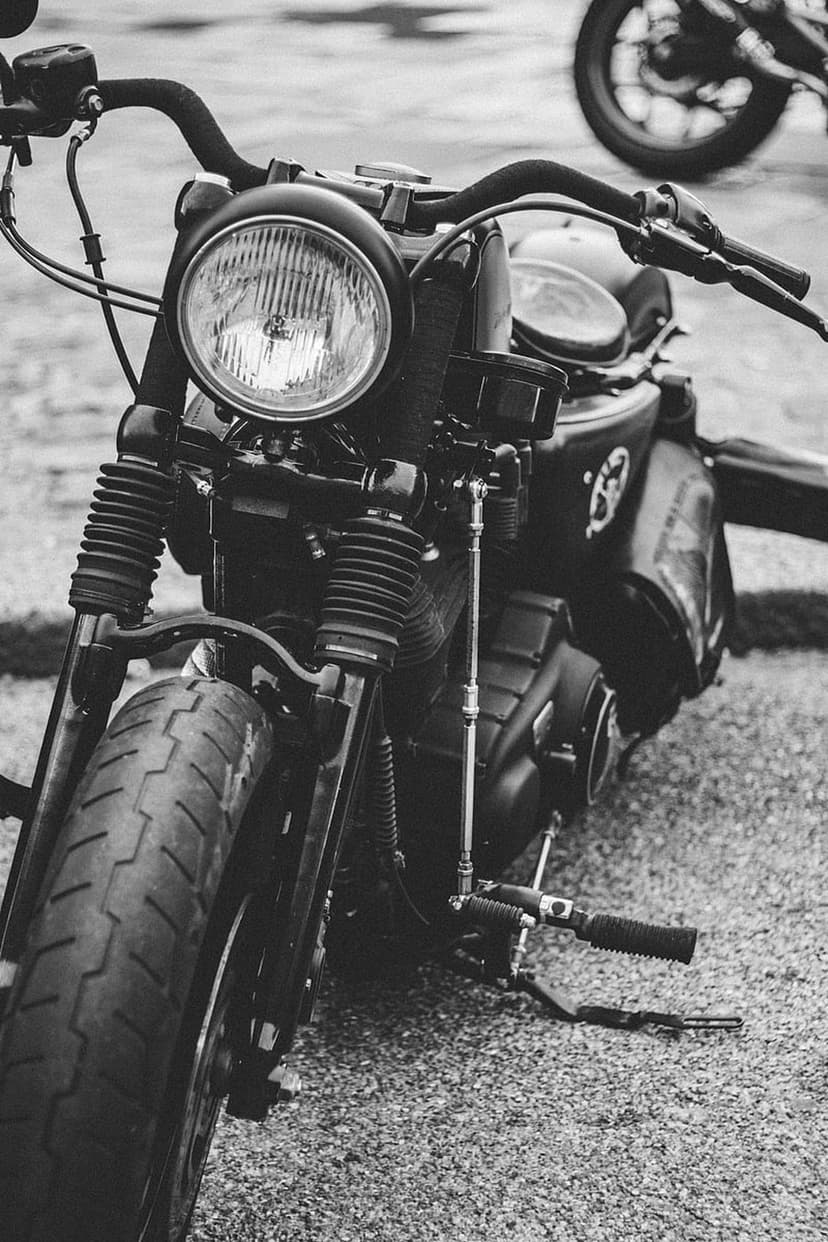 Vintage motorcycle headlight, ribbed forks, and a knobby tire are shown in a detailed black and white close-up.