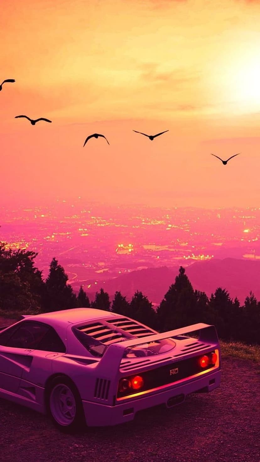 Pink sports car with glowing taillights parked on a dirt road during a vibrant orange and pink sunset.