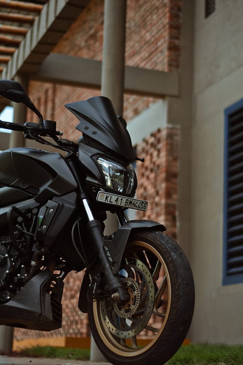 Matte black sports motorcycle with gold wheels and twin headlights parked in front of an urban brick building.