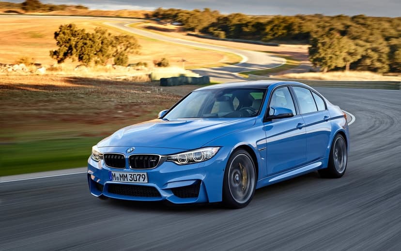Blue BMW M3 sports sedan driving fast on a curved racetrack during sunset with motion blurred wheels and hills.