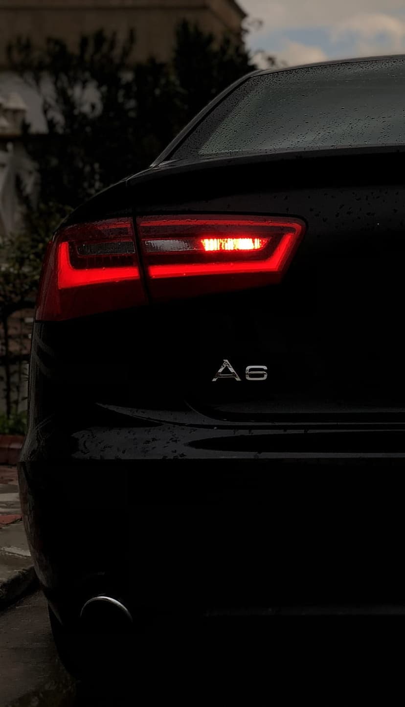 Audi A6 taillight glowing red with water droplets on a black car body during a rainy night with visible A6 badge.
