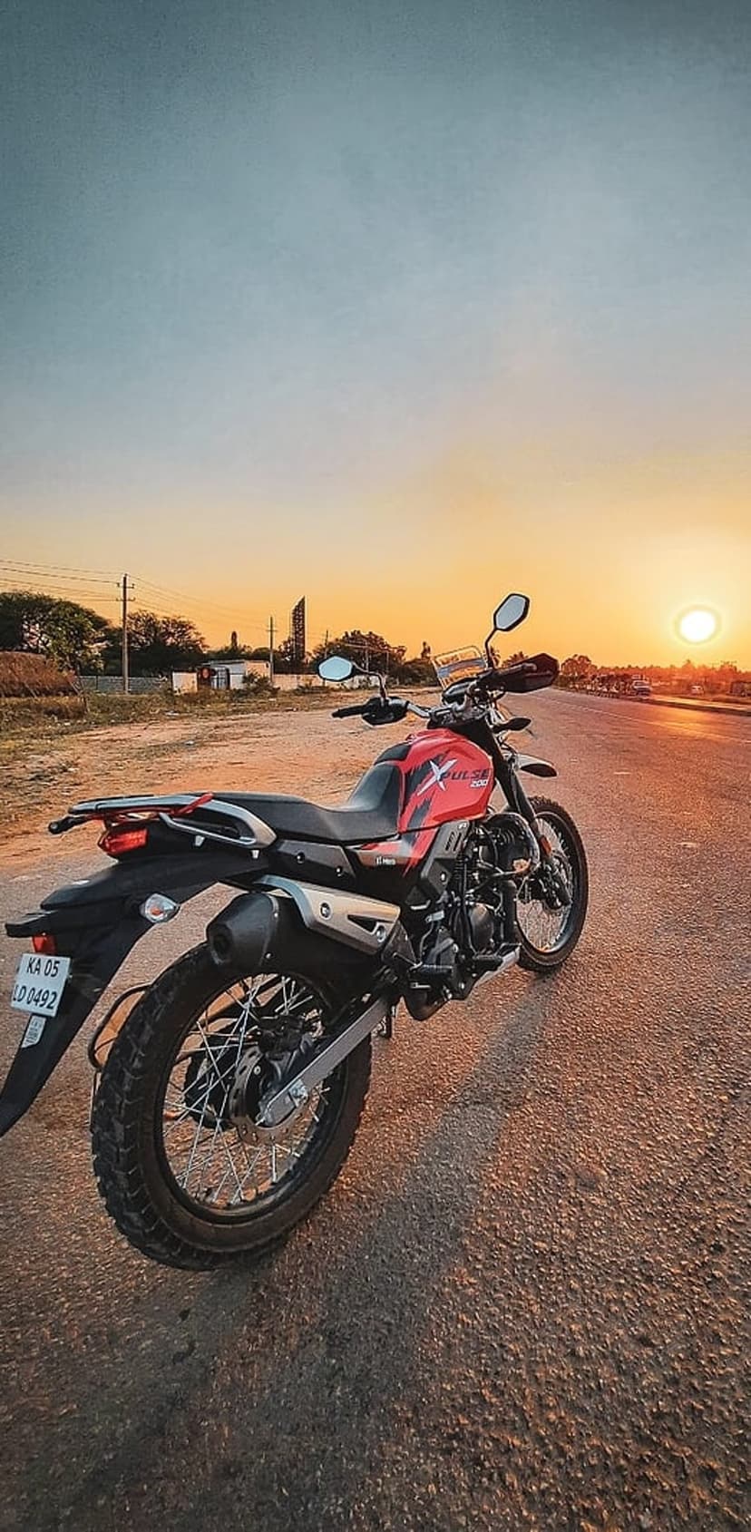 Red and black motorcycle parked on an asphalt road facing a bright orange sunset during the golden hour.