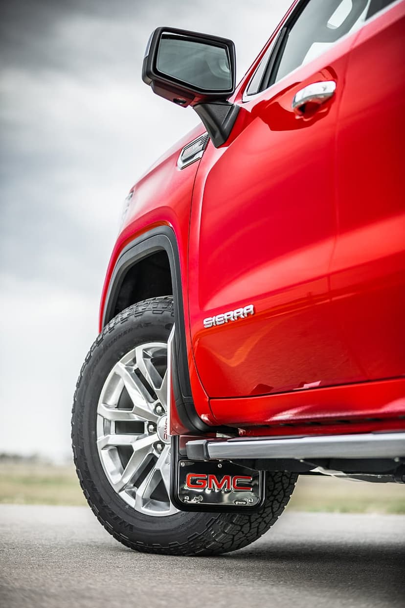 Red GMC Sierra pickup truck front wheel and fender with a black logo-embossed mud flap and chrome wheels.