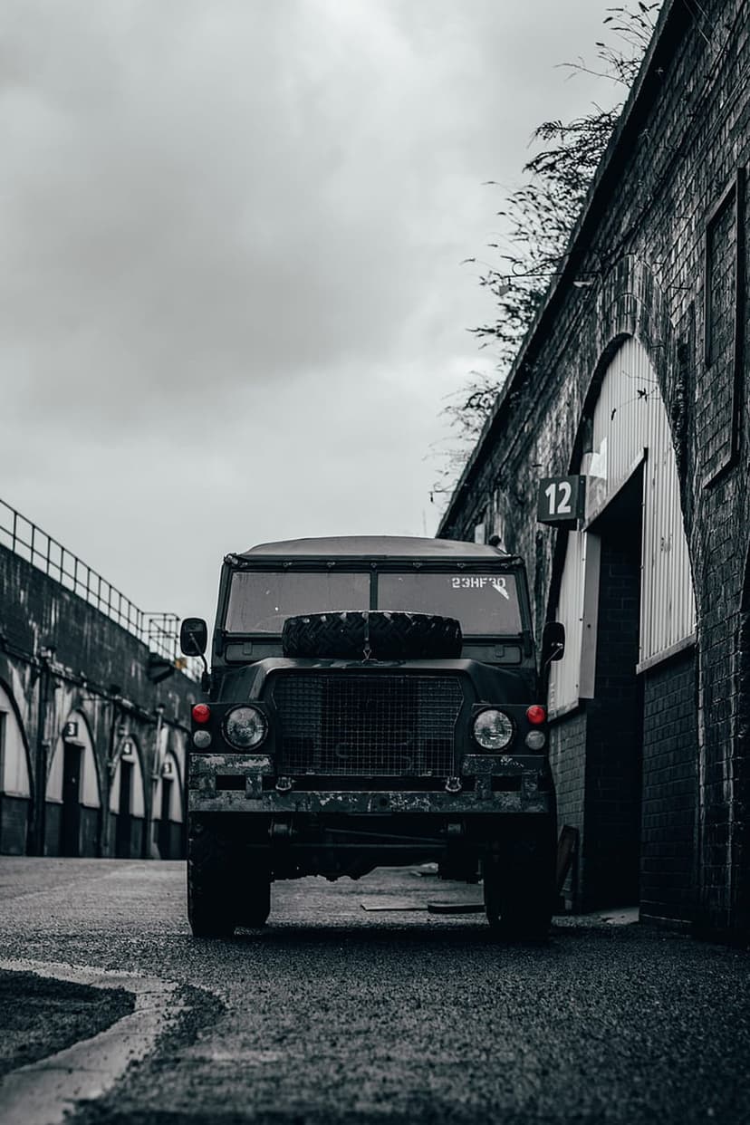 Land Rover Defender with a hood spare tire parked in a dark brick tunnel with arched doorways in monochrome.