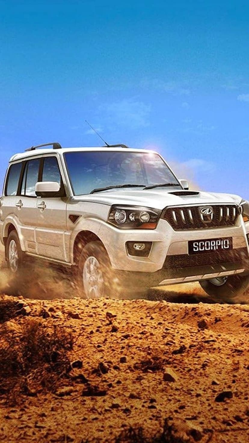 White Mahindra Scorpio SUV drives through golden desert sand under a clear blue sky during a sunny day.