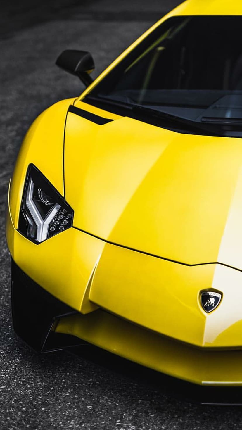 Yellow Lamborghini Aventador front end with sharp headlights and carbon fiber accents on a dark asphalt road.