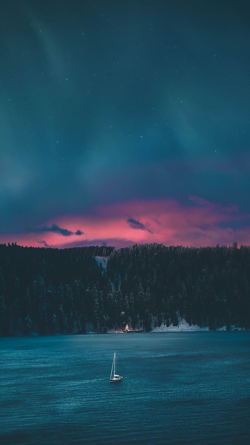 Lone sailboat on a dark lake under a green aurora borealis sky with snowy trees and twinkling stars at night.