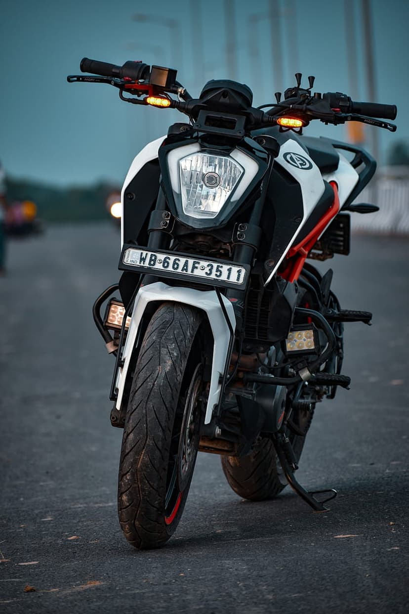 KTM Duke motorcycle with white and black fairings and orange accents parked on an asphalt road with blurred background.